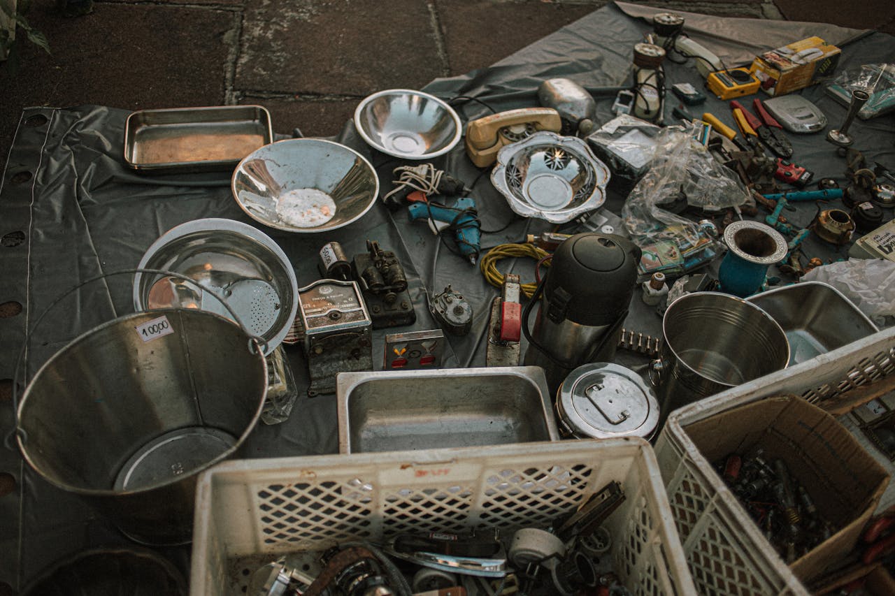 Assorted metal items and vintage tools displayed at an outdoor flea market on asphalt.